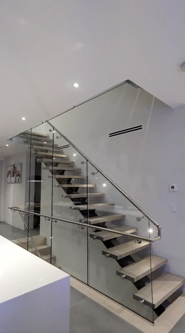 Floating open-riser stair with a full-height frameless glass guard beside a kitchen island