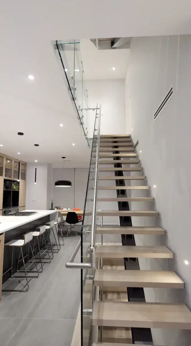 Looking up a floating stair with a glass guard and stainless handrail rising to the upper landing
