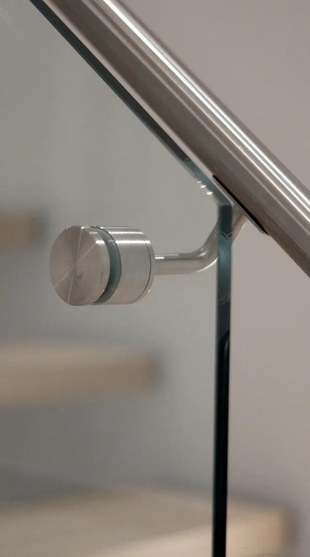 Close-up of a stainless glass-mount handrail bracket on tempered glass