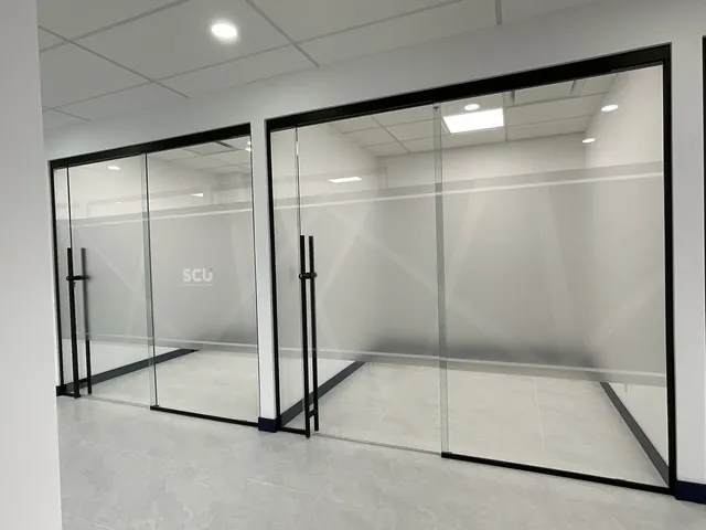 Two glass office fronts with black-framed swing doors and a frosted privacy band carrying the SCU logo