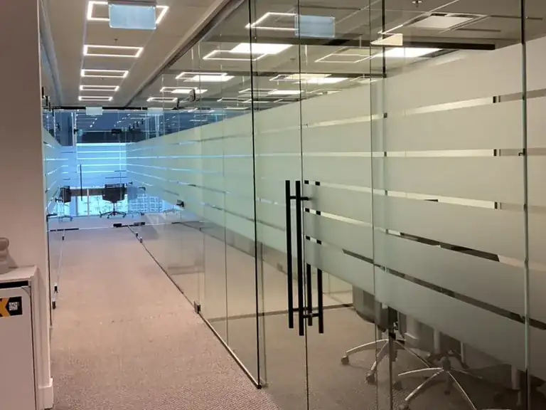 Long run of glass meeting-room walls with privacy film bands and double glass doors