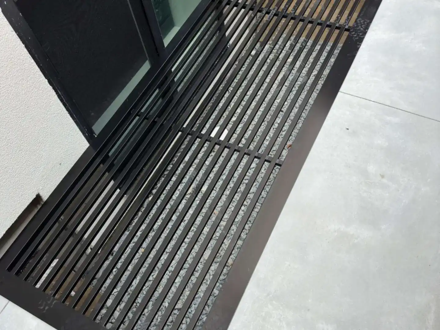 Black slatted window well cover beside a basement window